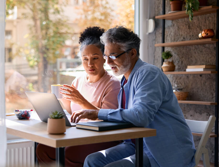 Mature couple using laptop and drinking coffee at home